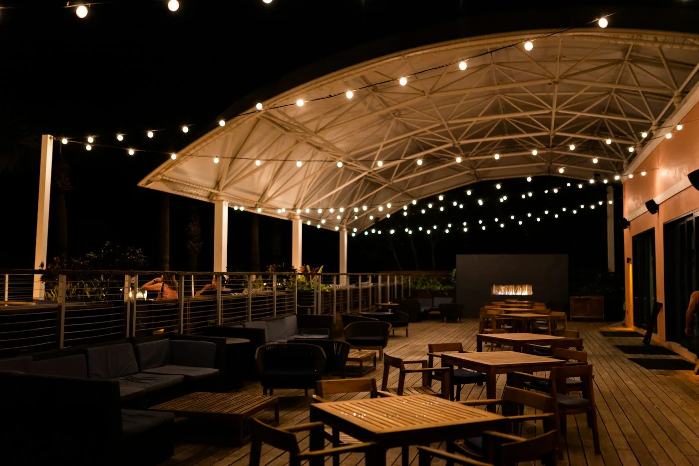 Festoon lighting strung across a venue deck and up over a canopy, set for an evening event.